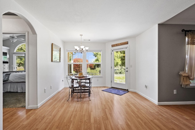 dining space with ceiling fan with notable chandelier, light wood-style floors, arched walkways, and baseboards