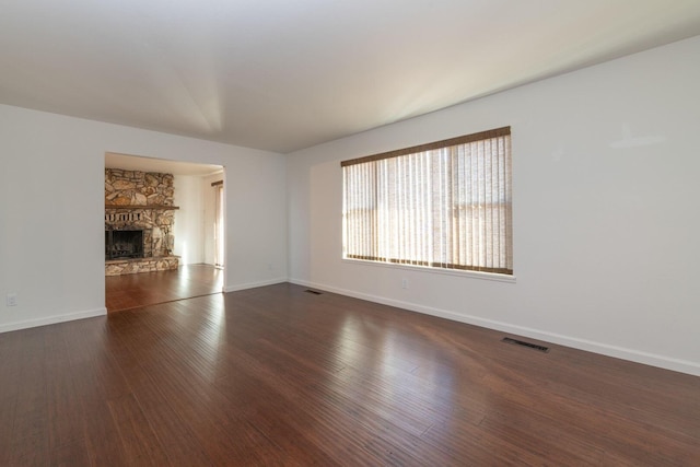 unfurnished living room featuring a stone fireplace and dark hardwood / wood-style flooring