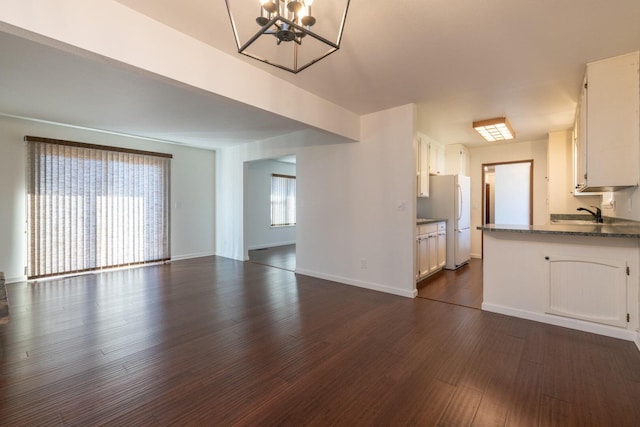 unfurnished living room with sink, an inviting chandelier, and dark hardwood / wood-style flooring