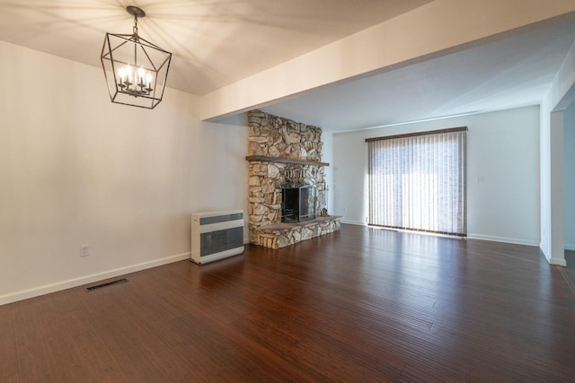 unfurnished living room featuring a stone fireplace, dark wood-type flooring, heating unit, and an inviting chandelier