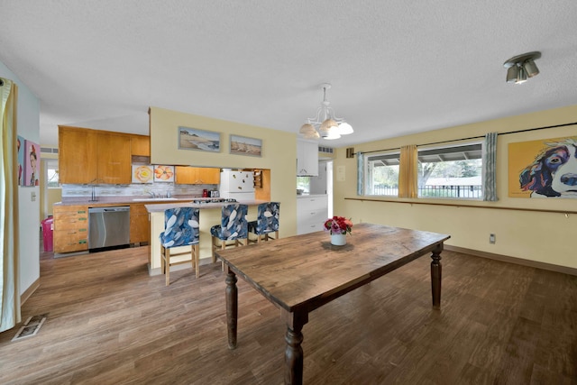 dining space with sink, a textured ceiling, a notable chandelier, and light wood-type flooring