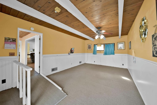 carpeted empty room featuring beamed ceiling, ceiling fan, and wood ceiling