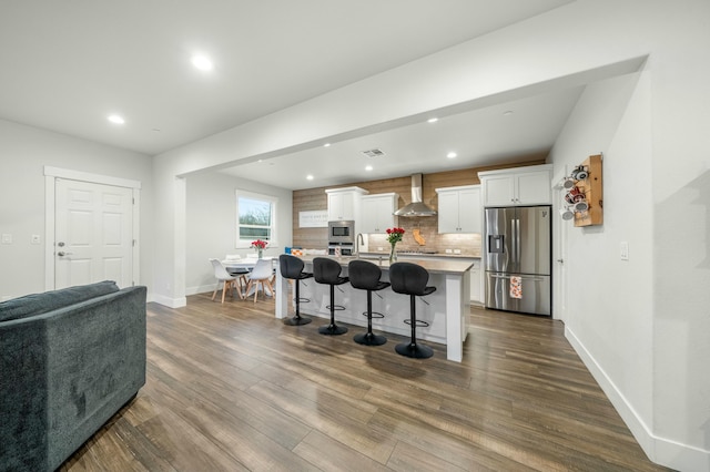 kitchen featuring a breakfast bar, appliances with stainless steel finishes, white cabinets, a large island, and wall chimney range hood