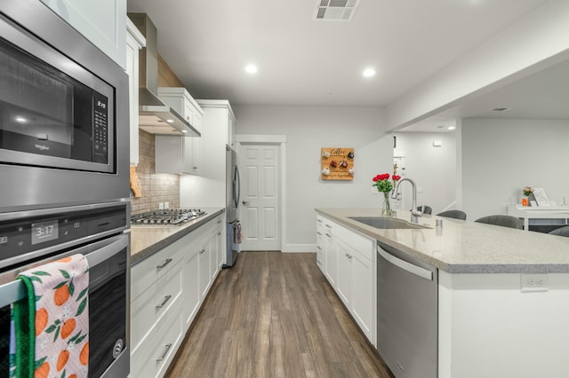 kitchen featuring wall chimney exhaust hood, sink, white cabinetry, stainless steel appliances, and a kitchen island with sink