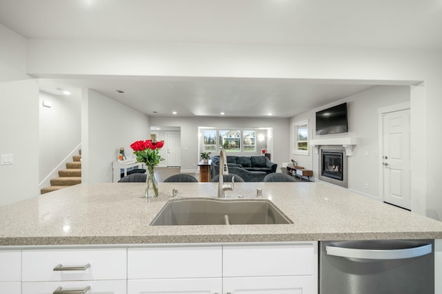 kitchen featuring light stone counters, sink, stainless steel dishwasher, and white cabinets