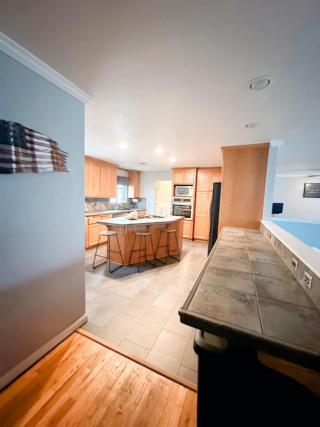 kitchen featuring black refrigerator, a kitchen bar, a kitchen island, stainless steel oven, and light wood-type flooring