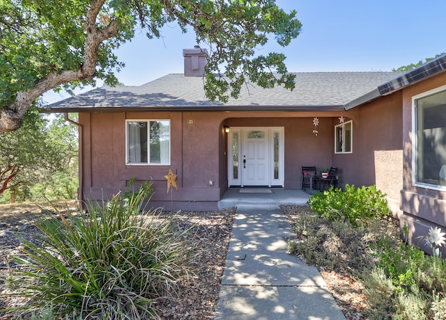 entrance to property with a porch, a chimney, a shingled roof, and stucco siding