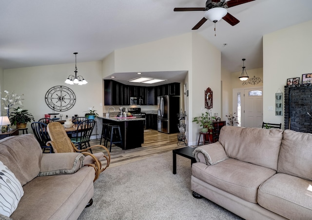 living room featuring high vaulted ceiling, light wood-style flooring, and ceiling fan with notable chandelier