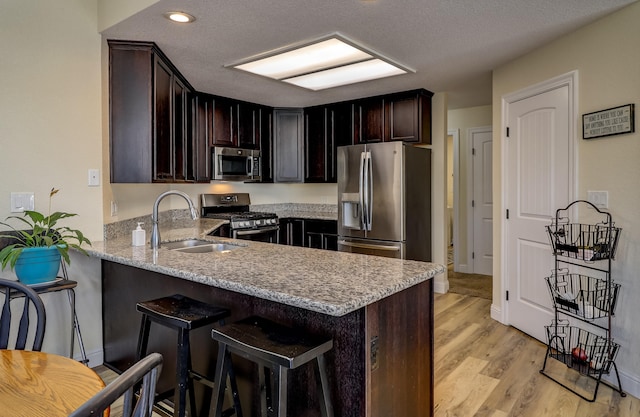 kitchen with a breakfast bar area, light wood finished floors, stainless steel appliances, a sink, and a peninsula