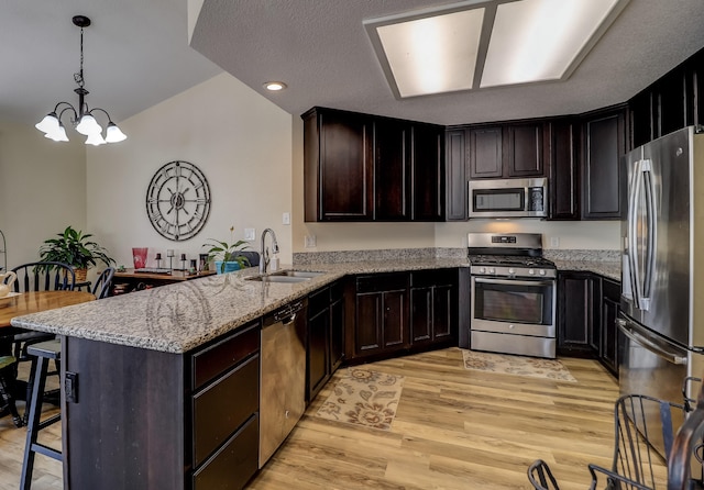 kitchen with light stone counters, stainless steel appliances, light wood-style floors, a sink, and a peninsula