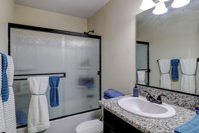 full bathroom featuring toilet, a textured wall, enclosed tub / shower combo, and vanity