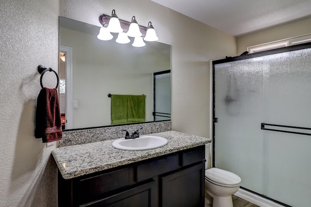 full bathroom featuring toilet, a stall shower, a textured wall, and vanity