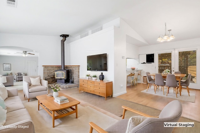 living room featuring ceiling fan with notable chandelier, light hardwood / wood-style floors, vaulted ceiling, and a wood stove