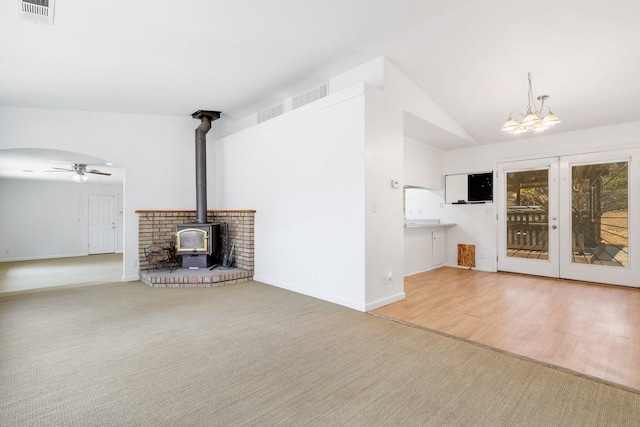 unfurnished living room featuring french doors, lofted ceiling, a wood stove, carpet floors, and ceiling fan with notable chandelier