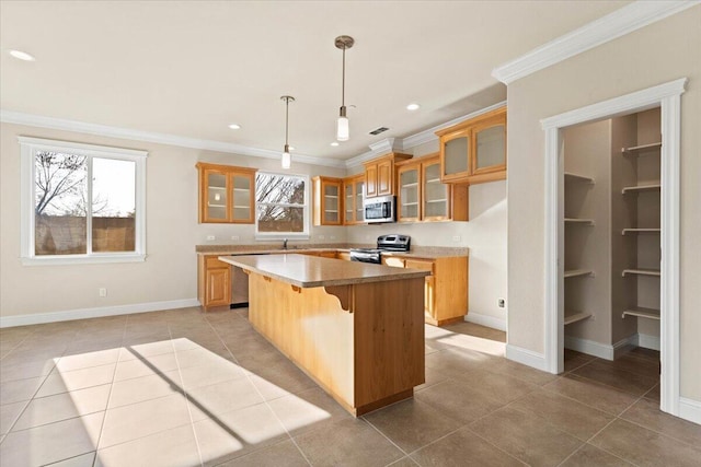 kitchen with decorative light fixtures, light tile patterned floors, ornamental molding, a kitchen island, and stainless steel appliances