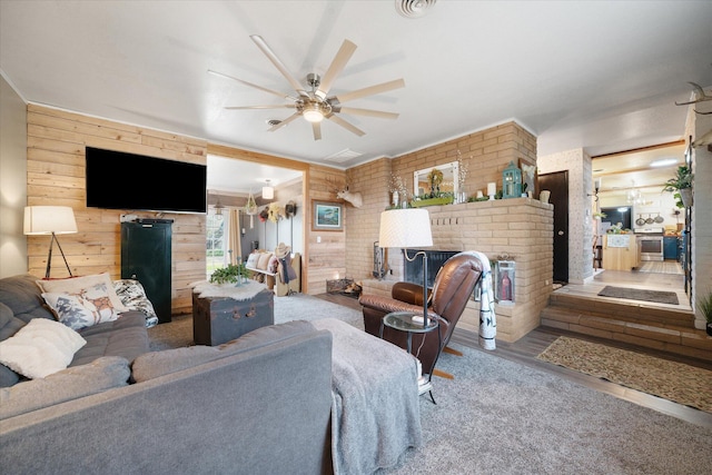 living room featuring wooden walls, ceiling fan, wood-type flooring, and a fireplace