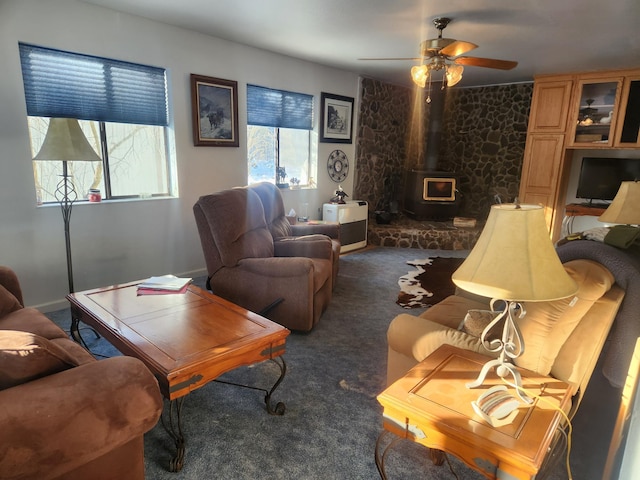 living room featuring ceiling fan, a wood stove, and dark carpet