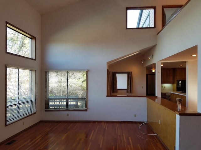 unfurnished living room with plenty of natural light, dark hardwood / wood-style floors, and a high ceiling