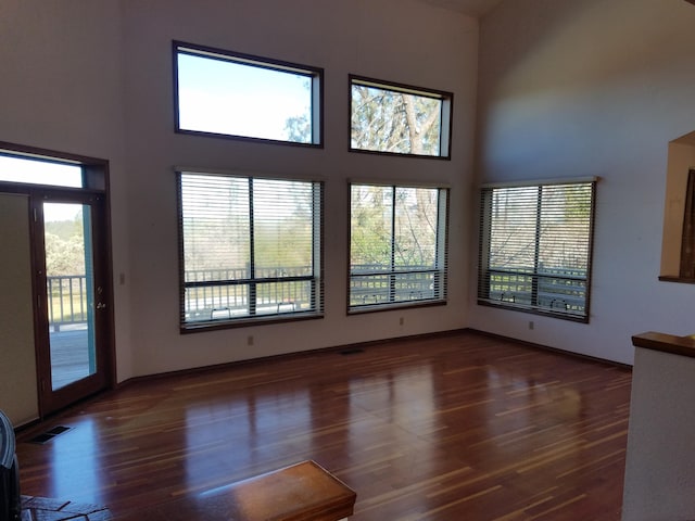 unfurnished living room featuring dark wood-type flooring, a healthy amount of sunlight, and a high ceiling