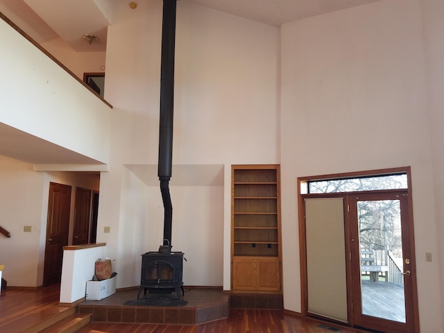 unfurnished living room with a high ceiling, a wood stove, and dark hardwood / wood-style flooring