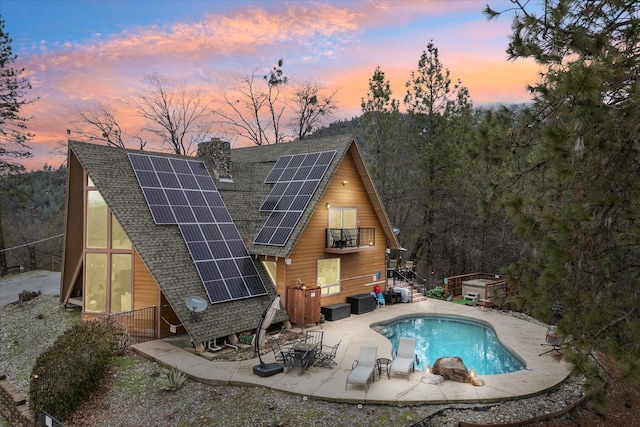 back house at dusk featuring a patio area and solar panels