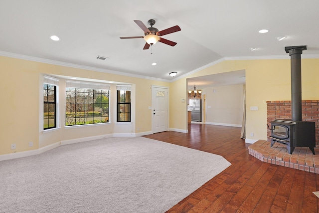 unfurnished living room with ornamental molding, vaulted ceiling, a wood stove, and ceiling fan with notable chandelier