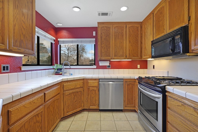 kitchen featuring stainless steel appliances, tile counters, sink, and light tile patterned floors