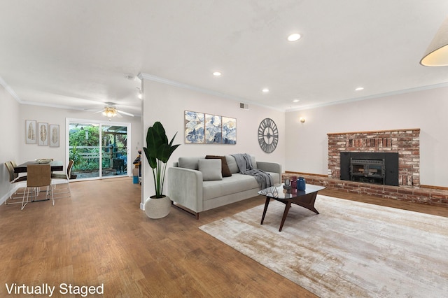 living room featuring crown molding, a brick fireplace, hardwood / wood-style flooring, and ceiling fan