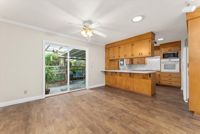 kitchen with crown molding, white oven, dark hardwood / wood-style floors, built in microwave, and kitchen peninsula