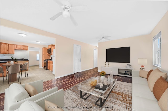 living area with light wood-type flooring, a ceiling fan, and baseboards