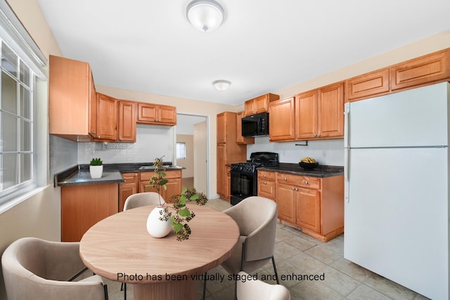 kitchen with light tile patterned floors, dark countertops, decorative backsplash, a sink, and black appliances