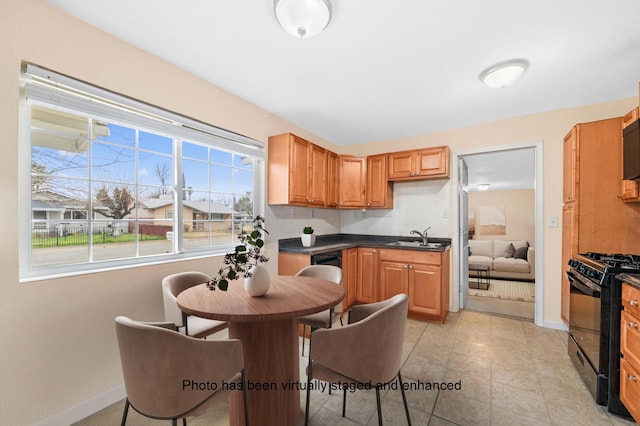 kitchen featuring dark countertops, backsplash, black range with gas cooktop, a sink, and baseboards