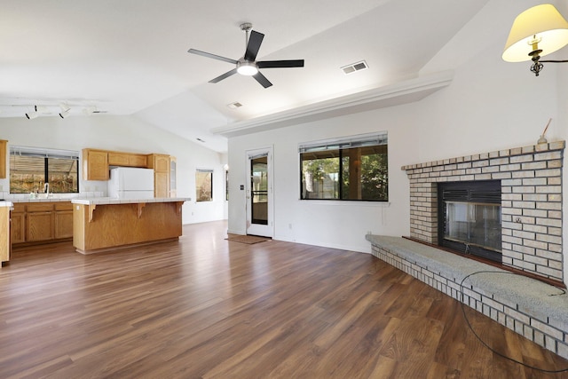 unfurnished living room featuring visible vents, dark wood finished floors, a ceiling fan, lofted ceiling, and a brick fireplace