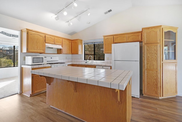 kitchen with white appliances, tile countertops, a kitchen island, under cabinet range hood, and a sink