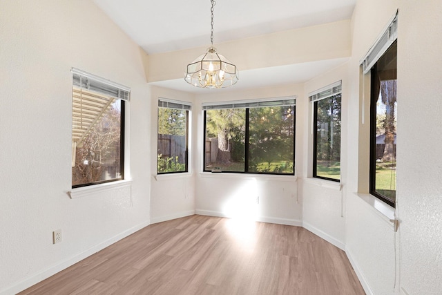 unfurnished room featuring light wood-style floors, vaulted ceiling, a notable chandelier, and baseboards