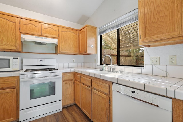 kitchen with tile countertops, under cabinet range hood, white appliances, dark wood-type flooring, and a sink