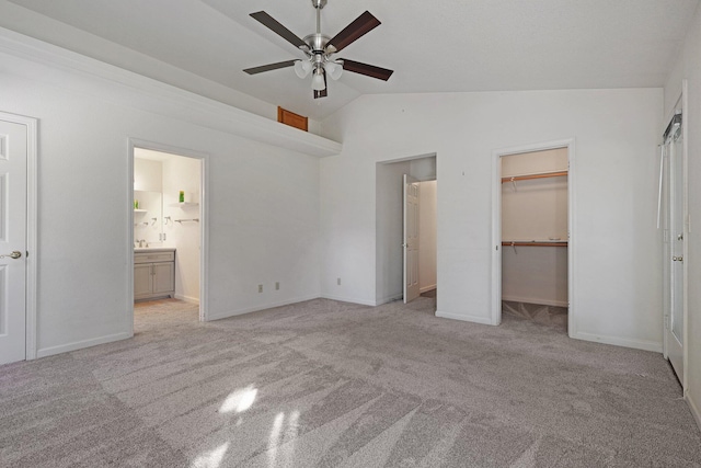 unfurnished bedroom featuring lofted ceiling, a spacious closet, light carpet, and ensuite bath