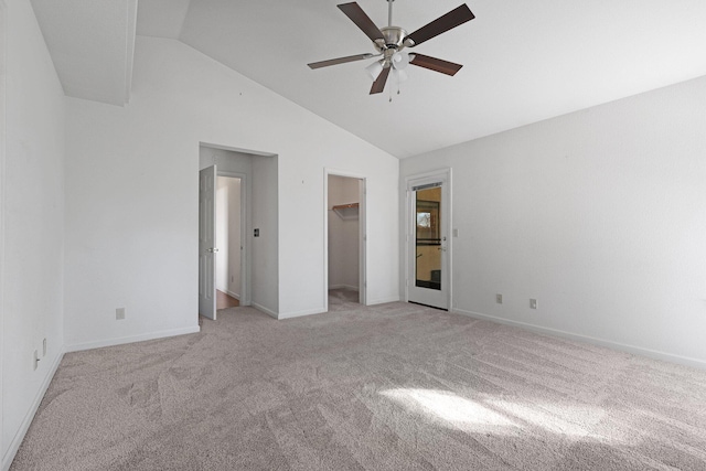 unfurnished bedroom with baseboards, a ceiling fan, light colored carpet, a walk in closet, and high vaulted ceiling