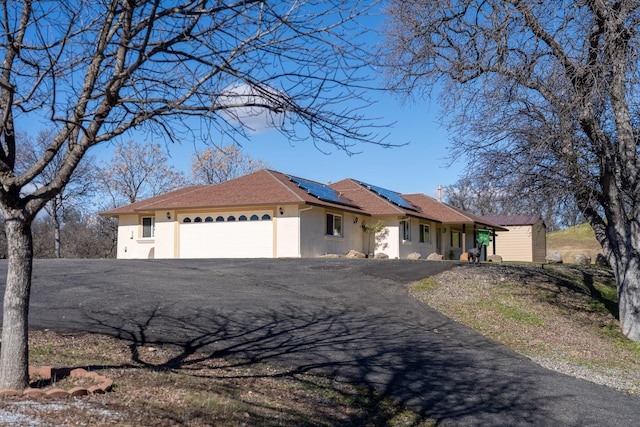 view of front of house featuring stucco siding, driveway, an attached garage, and solar panels