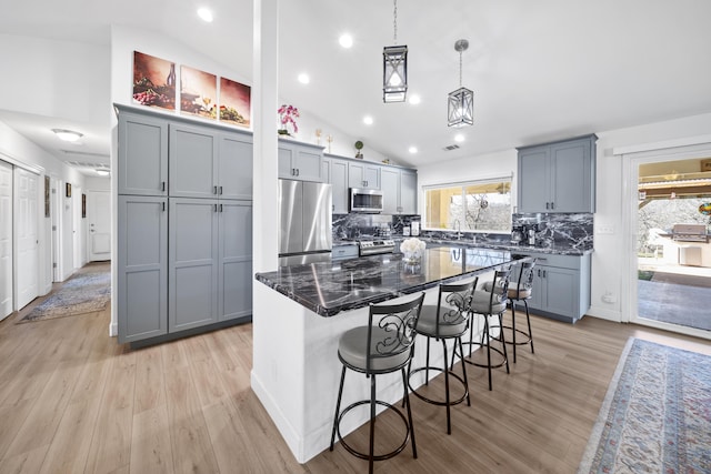 kitchen with hanging light fixtures, appliances with stainless steel finishes, a kitchen island, dark stone counters, and a kitchen breakfast bar