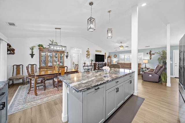 kitchen featuring hanging light fixtures, visible vents, open floor plan, and dark stone countertops