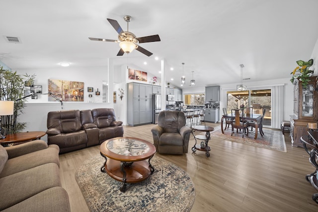 living room with light wood-type flooring, ceiling fan, visible vents, and vaulted ceiling