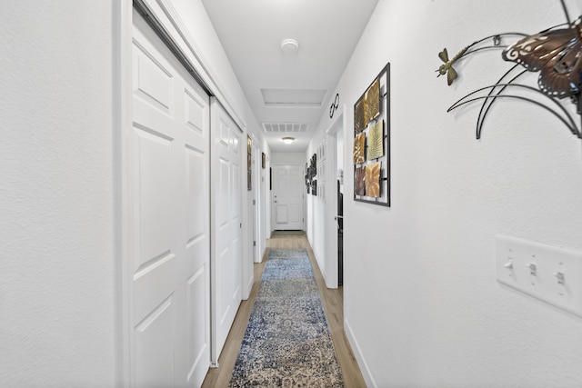 hall featuring light wood finished floors, baseboards, and visible vents