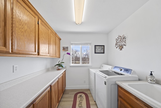 laundry area with cabinet space, baseboards, light wood-style flooring, independent washer and dryer, and a sink