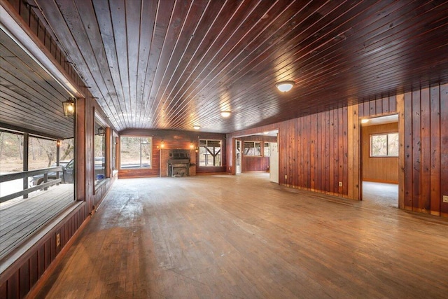 unfurnished living room featuring a fireplace, wood finished floors, wooden ceiling, and wood walls