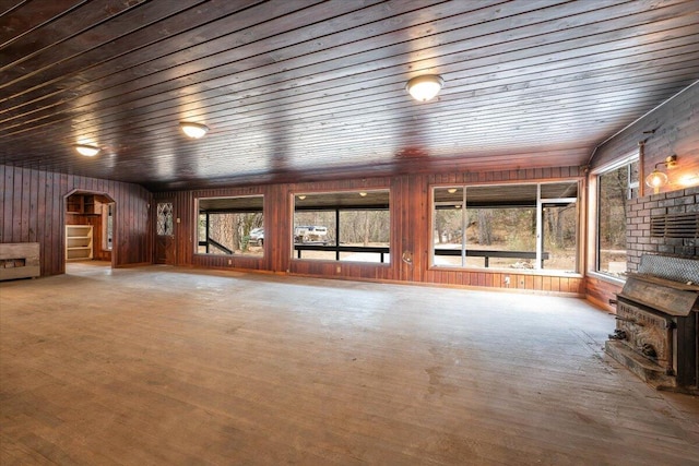 unfurnished living room with arched walkways, wood finished floors, wooden ceiling, and wood walls