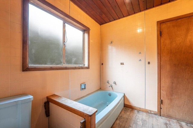 bathroom with wood finished floors, a tub, tile walls, toilet, and wooden ceiling