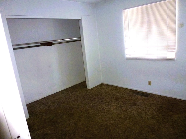 unfurnished bedroom featuring dark carpet and a closet