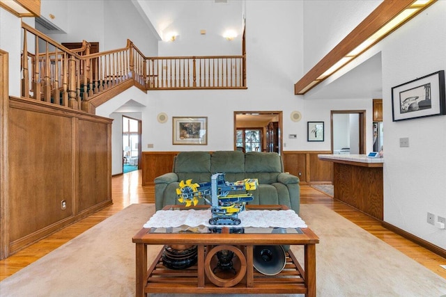 living room with a wealth of natural light, wooden walls, a high ceiling, and light wood-type flooring