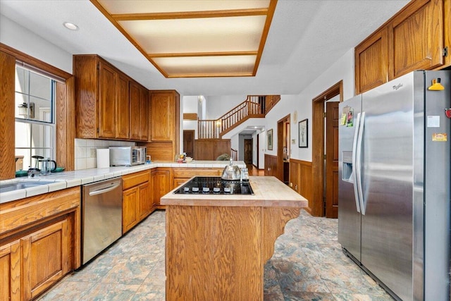 kitchen featuring sink, appliances with stainless steel finishes, wooden walls, a center island, and tile counters